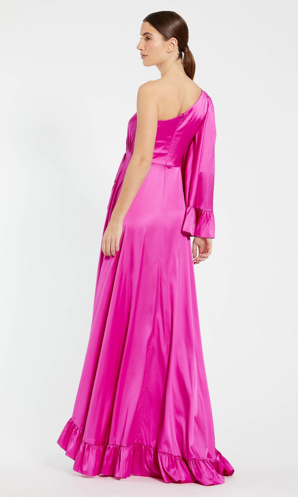 A woman in the Mac Duggal Long Formal Dress 55950, a bright magenta one-shoulder gown with ruffle details, stands facing away to showcase its elegant floor-length silhouette.